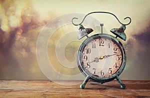 Image of vintage alarm clock on wooden table in front of abstract blured background. retro filtered