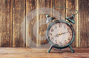 Image of vintage alarm clock on wooden table in front of wooden background. retro filtered photo