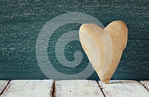 Image of vintage fabric heart on wooden table in front of blackboard