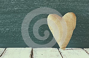 Image of vintage fabric heart on wooden table in front of blackboard