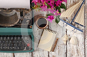 Image of vintage typewriter, blank notebook, cup of coffee and old sailboat on wooden table