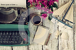 Image of vintage typewriter with phrase once upon a time, blank notebook, cup of coffee and old sailboat