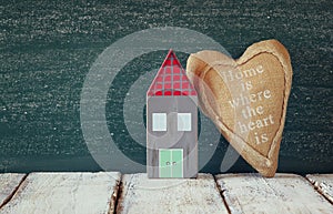 Image of vintage wooden colorful house and fabric heart on wooden table in front of blackboard