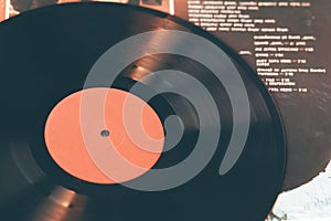 An image of a vinyl record that lies on the paper cover of a music album