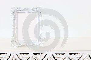 Image of white baroque vintage empty photo frame over wooden table. For mockup, can be used for photography montage