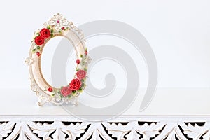 Image of white baroque vintage empty photo frame with red roses over wooden table. For mockup, can be used for photography montage
