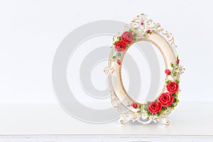 Image of white baroque vintage empty photo frame with red roses over wooden table. For mockup, can be used for photography montage