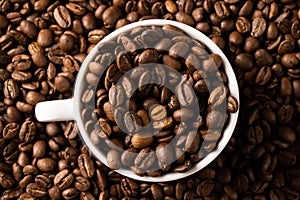 Image of white cup full of coffee beans on pile of coffee beans