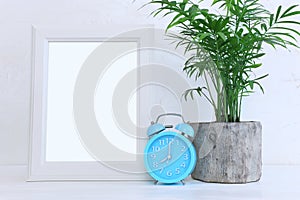 Image of white empty photo frame next to home plant over wooden table. For mockup, can be used for photography montage and text