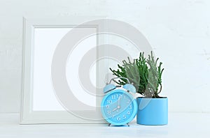 Image of white empty photo frame next to home plant over wooden table. For mockup, can be used for photography montage and text