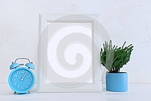 Image of white empty photo frame next to home plant over wooden table. For mockup, can be used for photography montage and text