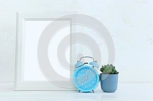 Image of white empty photo frame next to home plant over wooden table. For mockup, can be used for photography montage and text