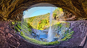 Wide angle in cave space behind waterfall over cliff edge with fall forest mountains behind