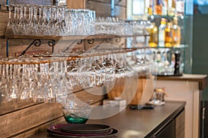 Image of wine glasses stacked on black metal hanging bar glass racks in a bar, nightclub or a restaurant with light shining