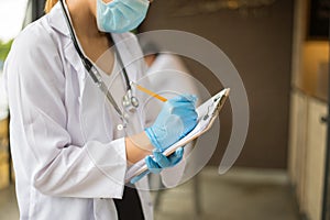 image of woman doctor in white coat with stethoscope and blue glove write report by pencil in a notebook on blur background of ho