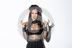 Image of woman in halloween costume looking like angry evil witch, cursing and clenching fists mad. Female in black