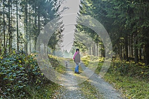 Image of a woman with her dog walking on a path in the middle of the forest
