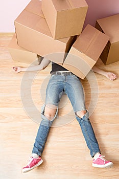 Image of woman in jeans lying under cardboard boxes