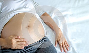 Image of A woman pregnant reclining on bed and touching or caressing her belly with hands.