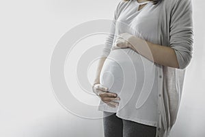 Image of A woman pregnant standing and touching or caressing her belly with hands.