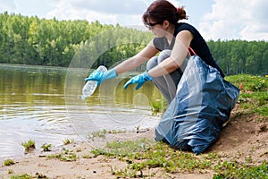 Image of woman in rubber gloves with dirty plastic bottle in her hands on river bank