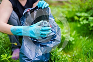 Image of woman in rubber gloves picking up dirty plastic bottle in bag on green lawn