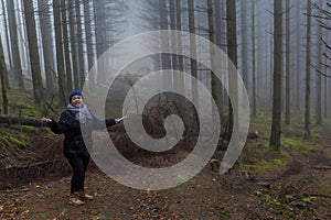 Image of a woman standing and asking if to continue on a path obstructed by fallen trees in the forest