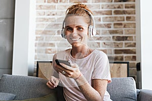 Image of woman using headphones and cellphone while sitting on couch