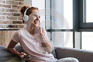 Image of woman using headphones and cellphone while sitting on couch