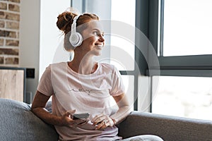 Image of woman using headphones and cellphone while sitting on couch