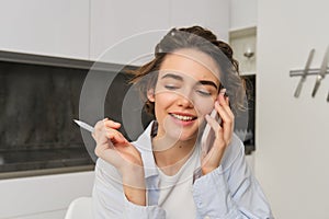 Image of woman working from home, writing down information during a phone call, calling someone, using smartphone