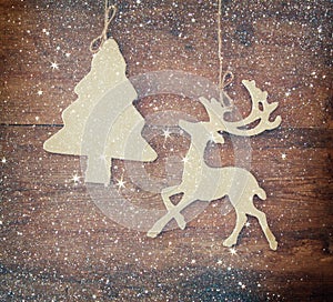 Image of wooden decorative christmas tree and reindeer hanging on a rope over wooden background with glitter overlay