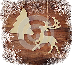 Image of wooden decorative christmas tree and reindeer hanging on a rope over wooden background with snowflake overlay.