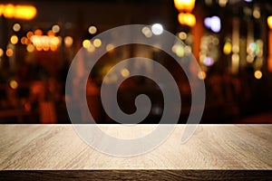 Image of wooden table in front of abstract blurred restaurant lights background