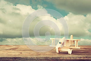 Image of wooden toy airplane over wooden table against cloudy sky. retro style image