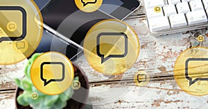 Image of yellow digital message icons flying up over electronic devices on wooden background
