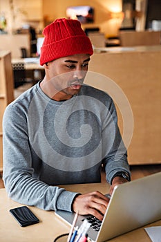 Image of young african american man using laptop while working in office