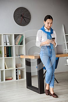Image of young asian woman using cellphone while working in office