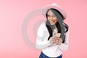 Image of young asian woman wearing hat smiling and holding cellphone