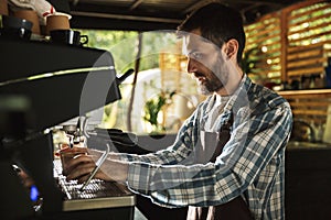 Image of young barista boy making coffee while working in cafe or coffeehouse outdoor