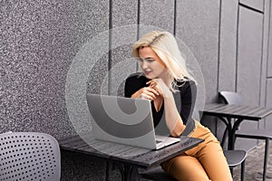 Image of young beautiful joyful woman smiling while working with laptop from outside