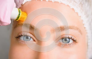 Image of a young beautiful woman dressed as a patient, lying on a couch in a cosmetology clinic.