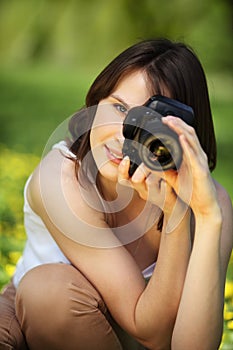 Image of young beautiful woman photographing in summer park