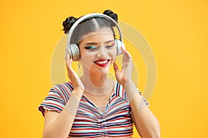 Image of young beautiful woman posing isolated over yellow background listening music with headphones