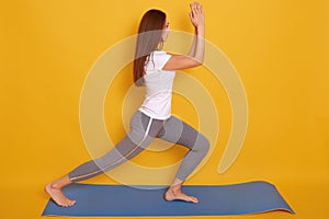 Image of young beautiful woman yoga posing isalated over yellow studio background, adorable female wearing white casual t shirt