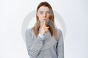 Image of young blond girl shushing at camera, telling a secret, asking to keep silent or quiet, showing taboo sign