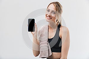 Image of young blond woman 20s dressed in sportswear with towel over neck using smartphone during workout in gym