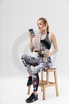 Image of young blond woman 20s dressed in sportswear using smartphone while sitting on chair after workout in gym