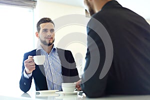 Image of young businessman with cup of coffee communicating with his colleague.