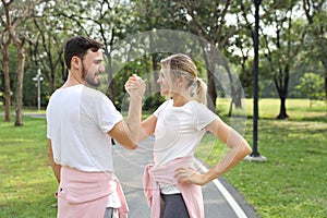 Image of young caucasian couple in white and pink sport dress with smiling and arm wrestling challenge in the park with green tree